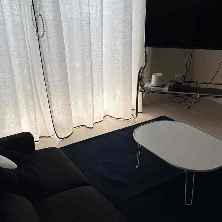 ホワイトとネイビーのトーンのリビング、黒いソファとネイビーのラグ、白いカーテンが並ぶモダンでシンプルなインテリア