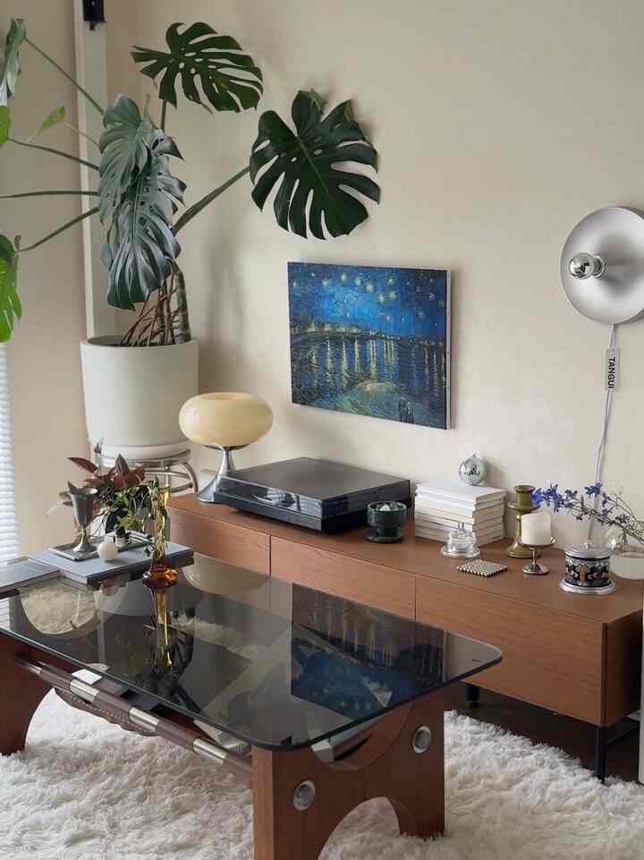 Natural-toned living room featuring silver accessories, large Monstera plants, and mid-century modern wooden furniture creating a stylish atmosphere