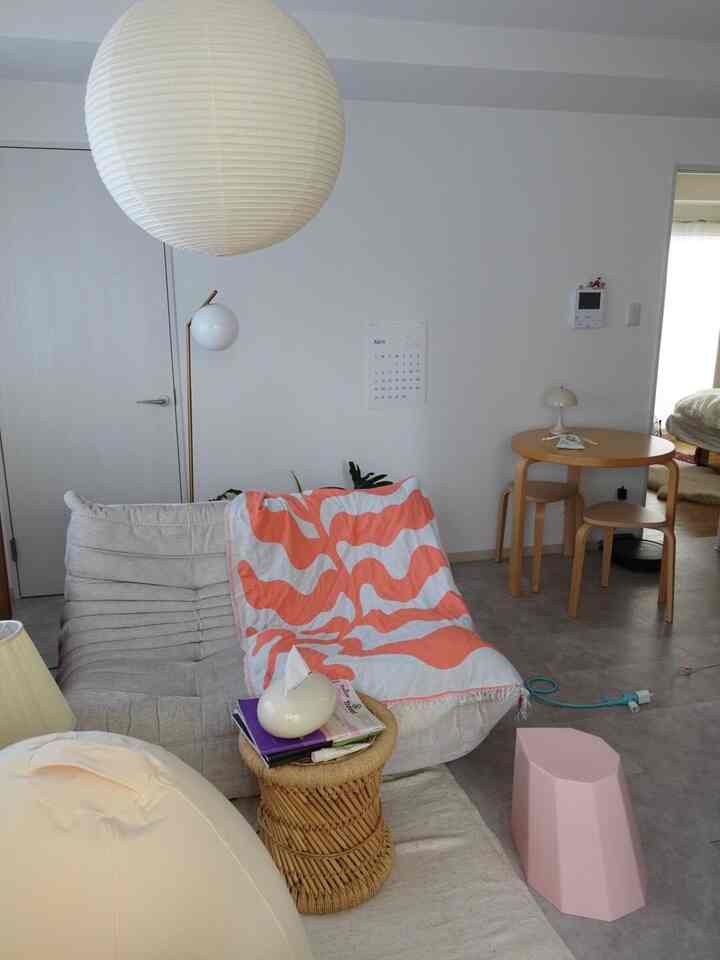 白い壁とナチュラルウッド家具のあるリビング、ベージュのソファにサンゴ色のスローがかかり、温かみのある印象的な空間