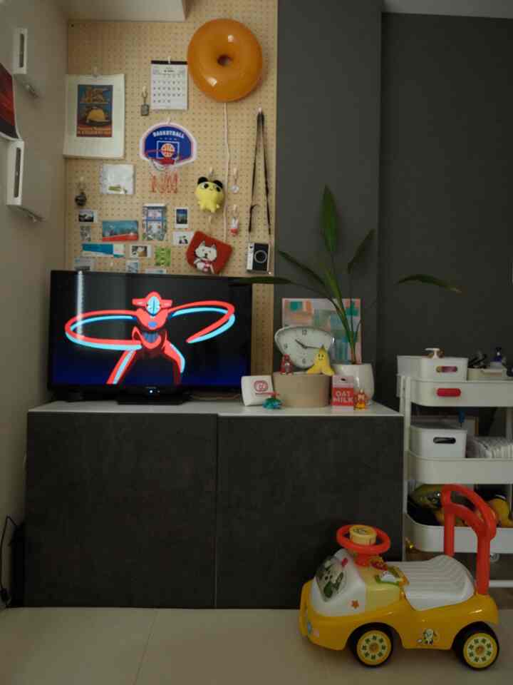 Living room with white floor and gray TV stand, featuring kids' toys and a pegboard wall in a cozy setting