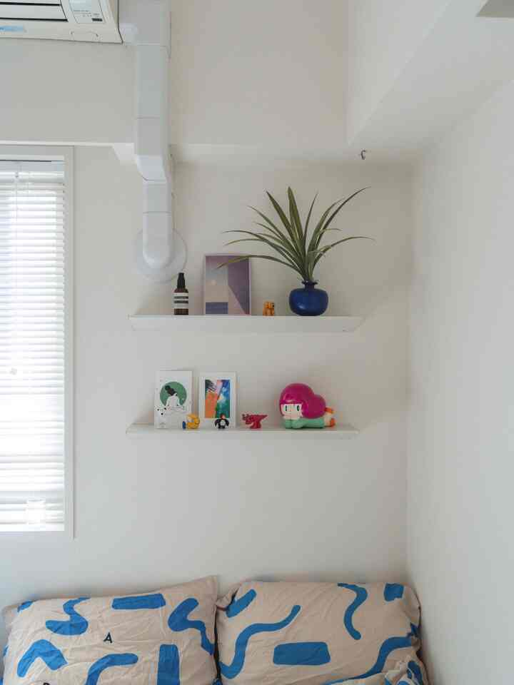 Bright white-toned bedroom with two neat wall shelves displaying a blue ceramic vase and assorted objets