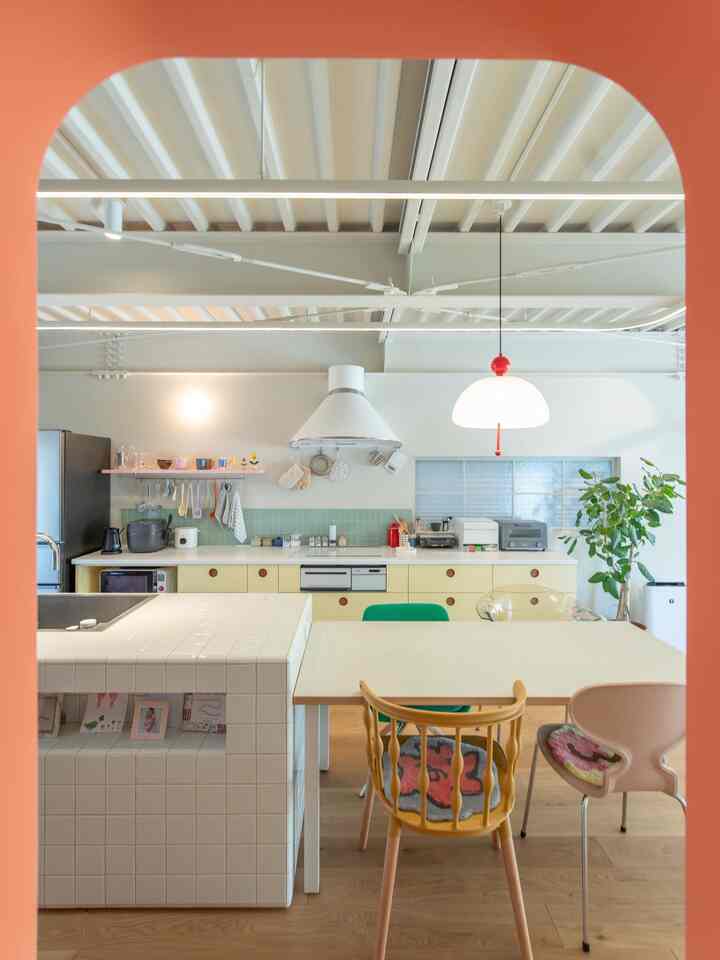 明るいホワイトと木目調のキッチンとダイニングルーム、カラフルなダイニングチェアとペンダントライトが配置された洗練された空間