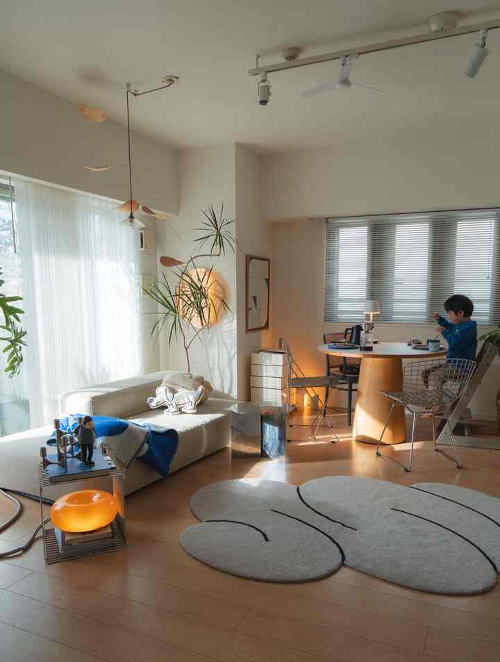 Natural style living room with white walls and wood tone flooring, featuring a sofa and dining table where a child is having breakfast in bright space