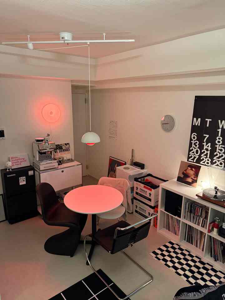 Small modern kitchen dining area featuring red accent lighting, espresso machine, and diverse chairs, creating a cozy ambiance