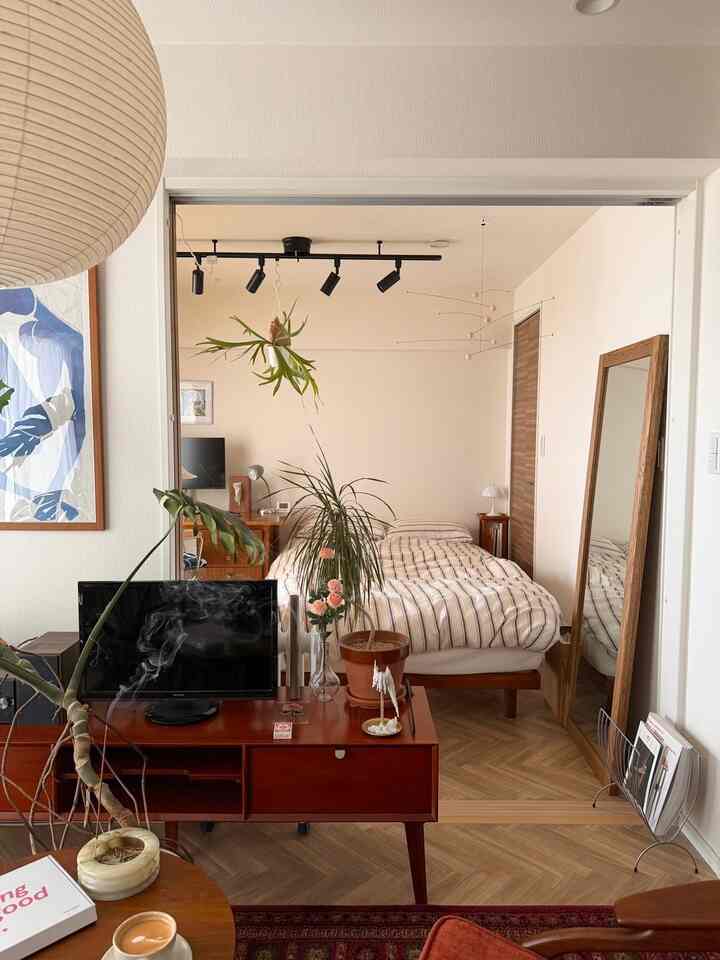 Natural-toned bedroom connected to living area, featuring wooden furniture and plants with a cozy atmosphere