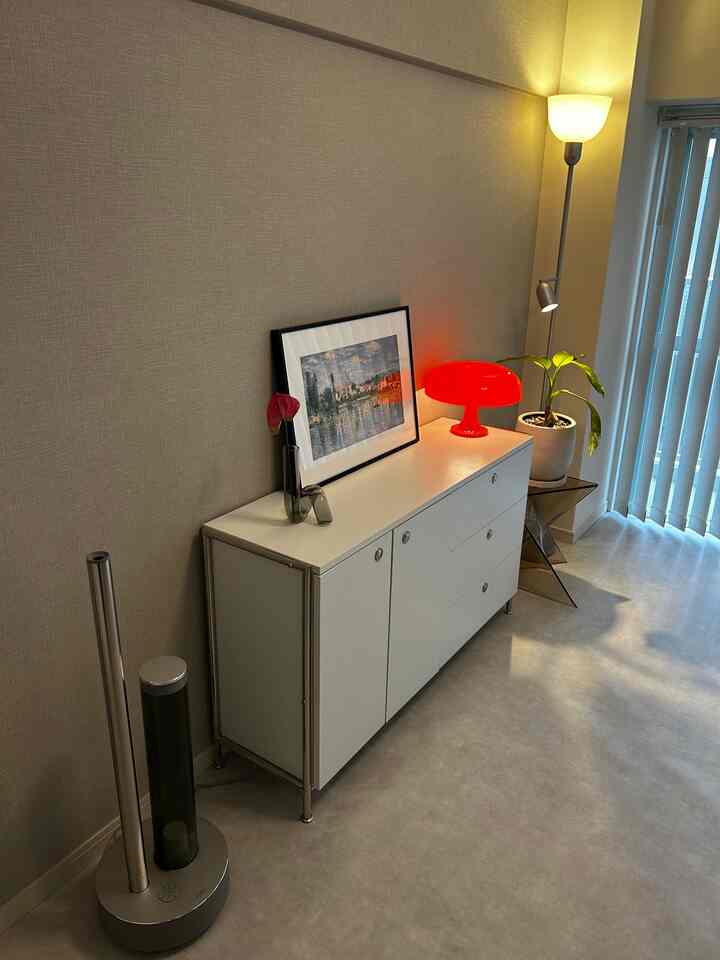 ブラウンの壁と白いサイドボードが配置されたモダンな照明空間、赤いテーブルランプと緑の植物が特徴的