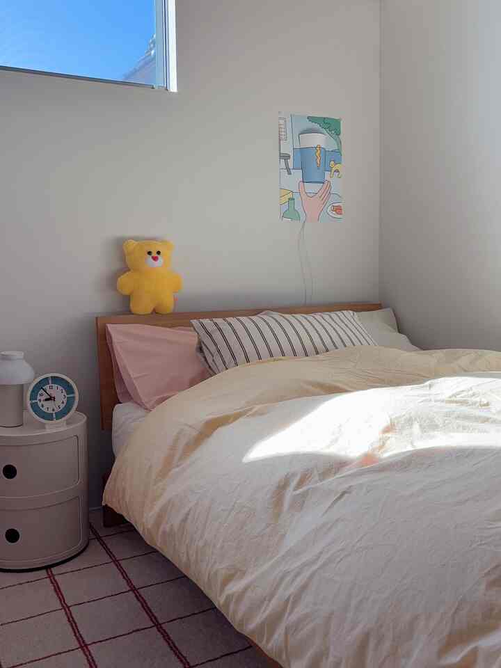 白とベージュのトーンが映える子供部屋、ナチュラルな木製ベッドと黄色いクマのぬいぐるみが配置された雰囲気のあるインテリア