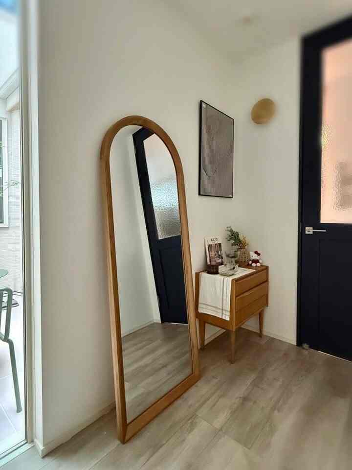 Natural wood tones and white walls in an entrance space featuring a full-length mirror and small wooden storage cabinet with cozy decor