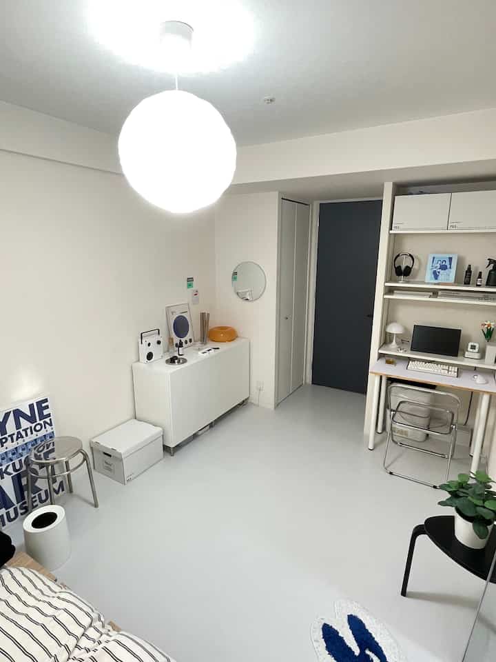 White-toned single household studio featuring a simple desk setup, stool, and transparent chair in a clean, minimal environment