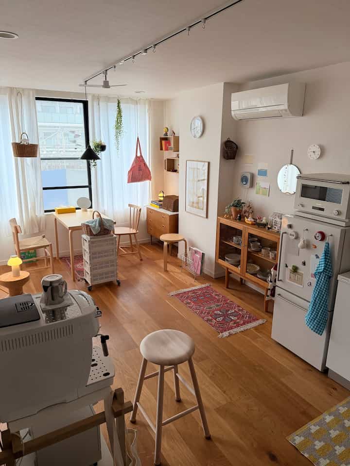 ナチュラルな色調のワンルームリビングとキッチン、木製家具とコーヒーメーカーが配置された雰囲気のある空間