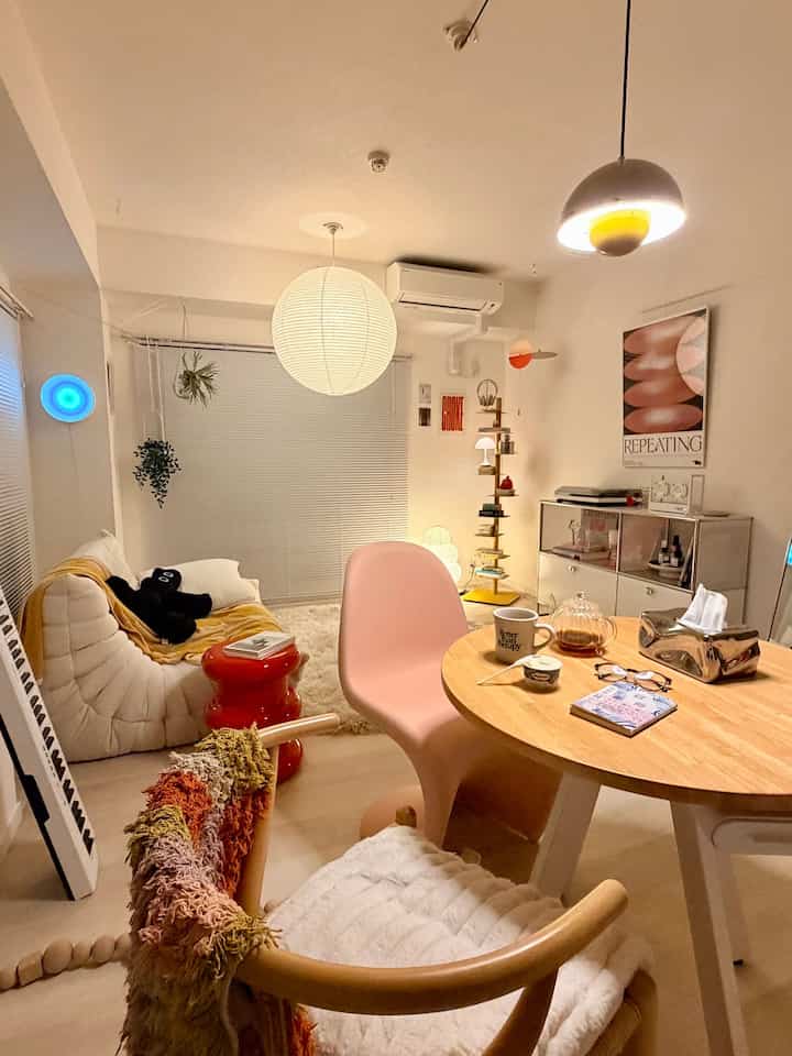 White and pink toned living and dining room featuring modern pendant lights and minimal furniture arrangement