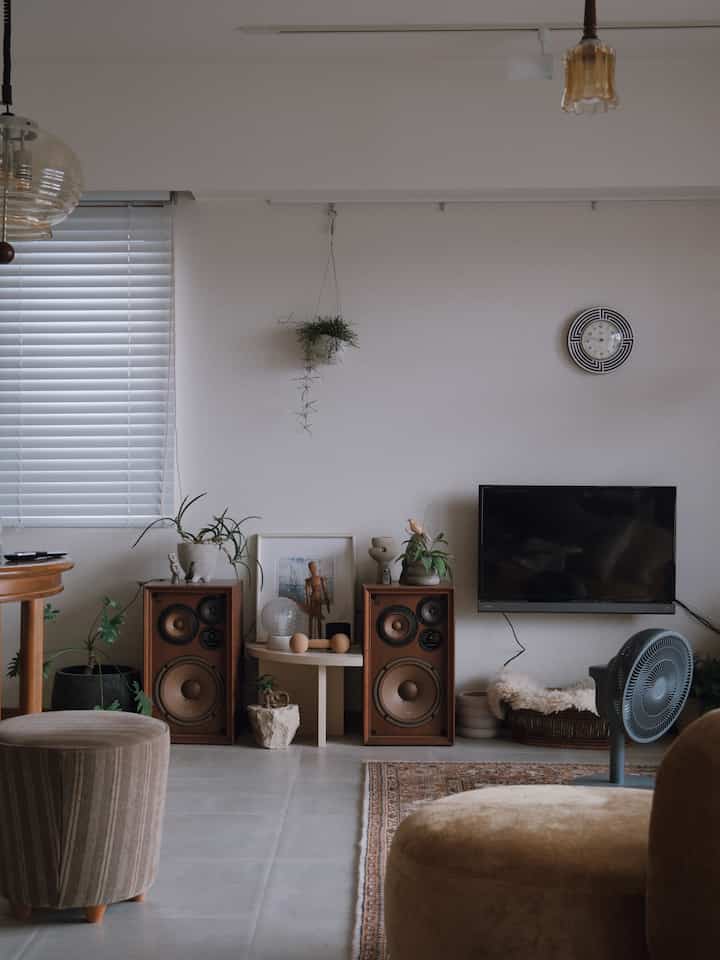 ブラウンとグレーのトーンのリビング、テレビやスピーカー、植物が配置された落ち着いた空間