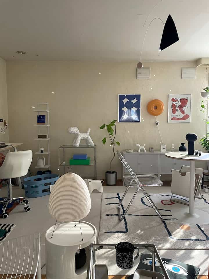 White-toned living room featuring mid-century modern furniture, various plants, and distinctive lighting creating a cozy atmosphere