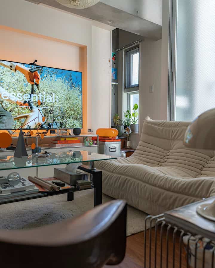 白とモダンなリビングルーム、大型テレビと金属製のテレビ台、ガラスのテーブル、快適なソファが配置された落ち着いた空間