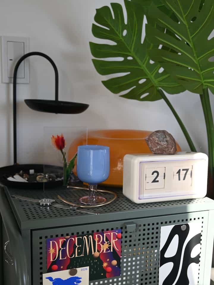 Calm space featuring gray shelf with green monstera plant, vintage clock, and blue glassware on top