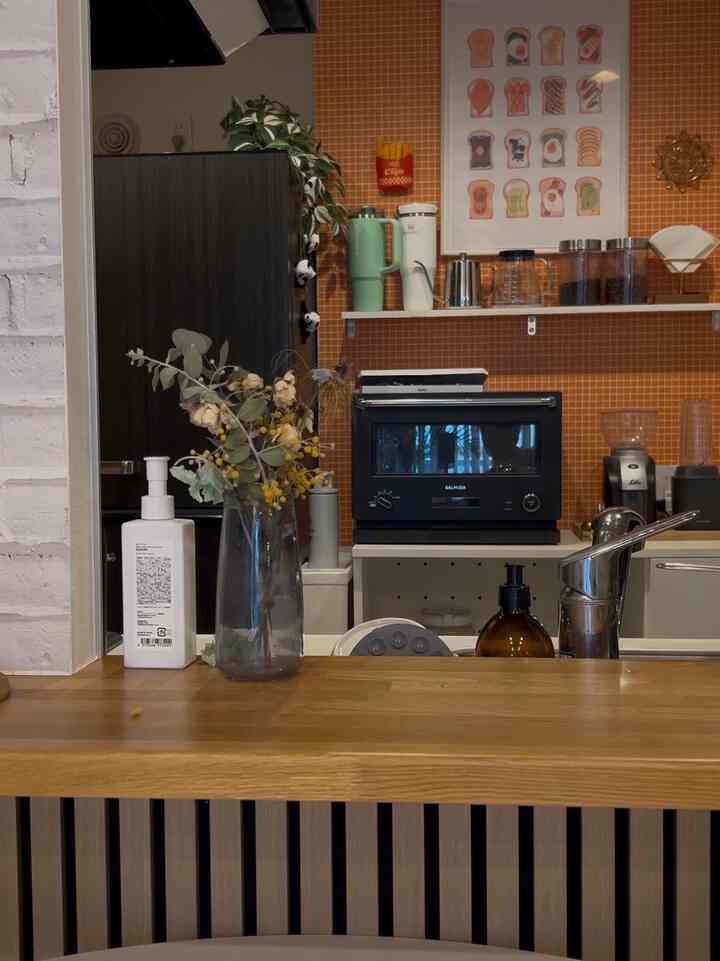 Kitchen space with orange tiled walls and wooden countertop, featuring Balmuda oven and coffee equipment in a natural atmosphere
