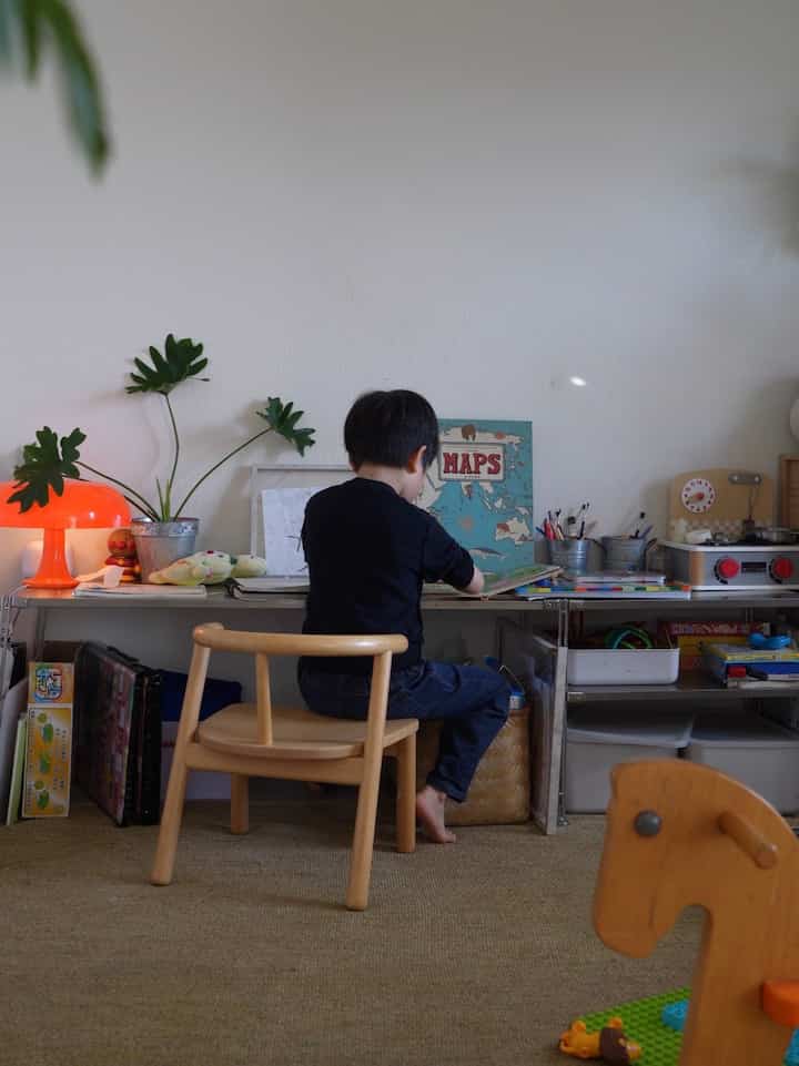 白い壁と木目調の家具が並ぶ子供部屋、中央の机で集中する子供がいる雰囲気のある空間