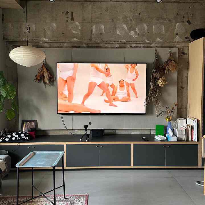 Modern living room with wood tones and black accents, featuring a wall-mounted TV and large pendant light on a textured concrete wall