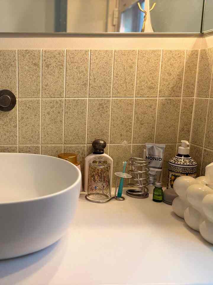 Bathroom space with beige tiled walls and white washbasin, featuring various toiletries and decorative objets creating a cozy interior