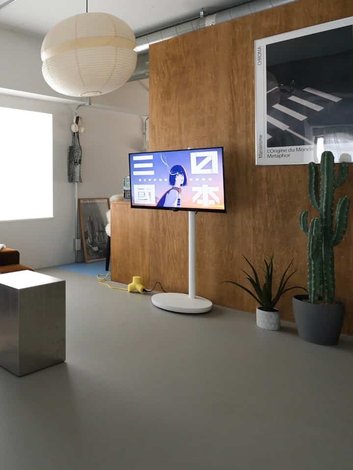 Modern living room in white and brown tones featuring a centrally placed TV and plants in a minimalistic setting