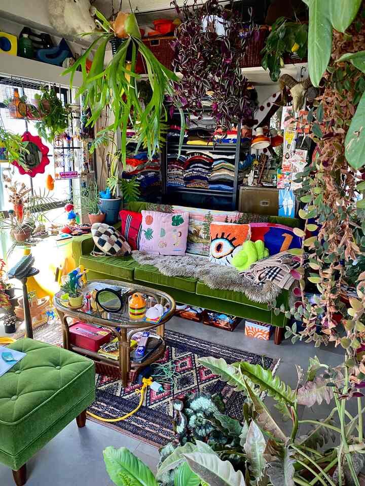 Living room with a green sofa and colorful cushions, lush plants arranged in a vintage style space