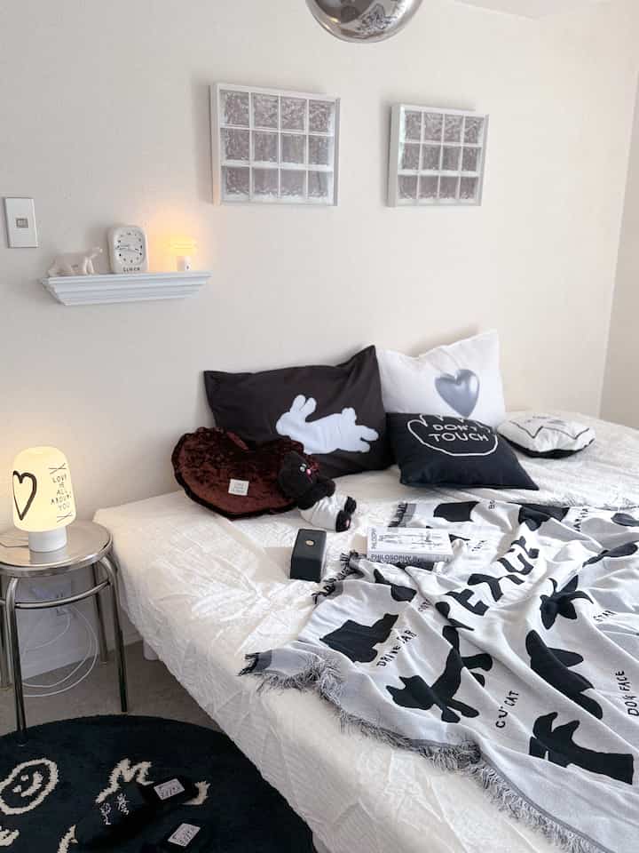White-tone bedroom featuring white walls and bedding with black and white pillows and throw, creating a simple atmosphere