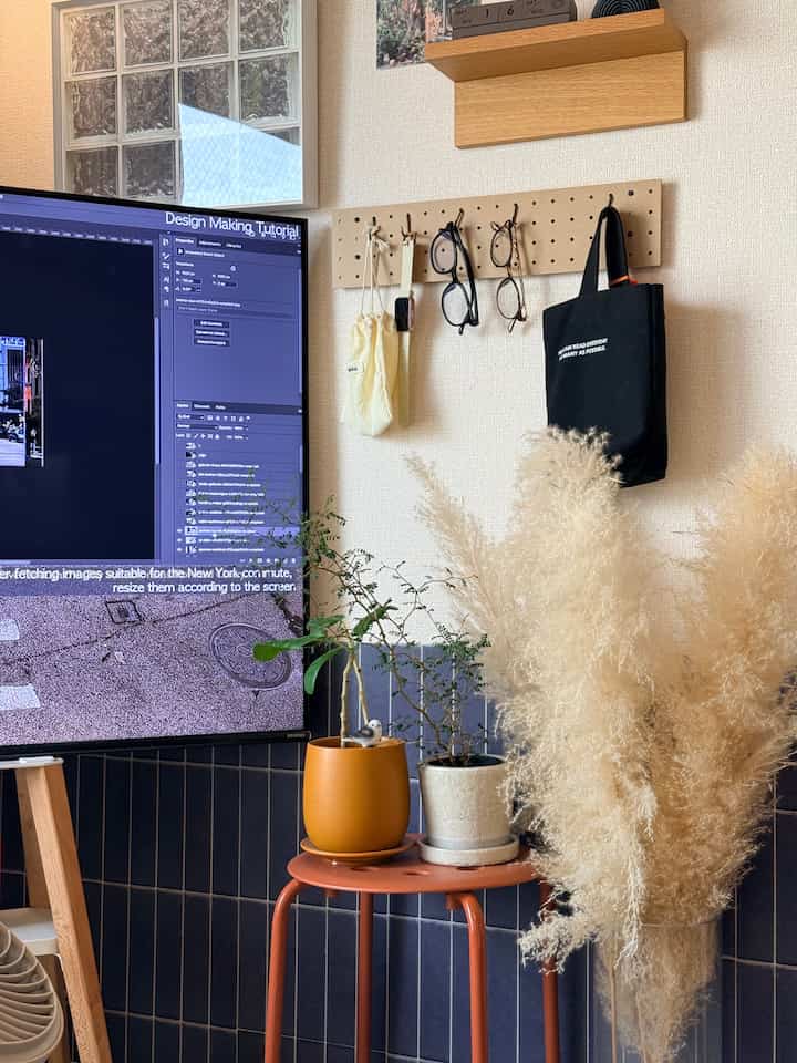 青いタイルの壁とオレンジのスツール、コンピュータモニターがあるシンプルなホームオフィスの空間