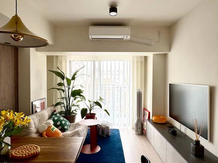 A white and natural tone living room featuring a sofa and plants with a simple and cozy atmosphere