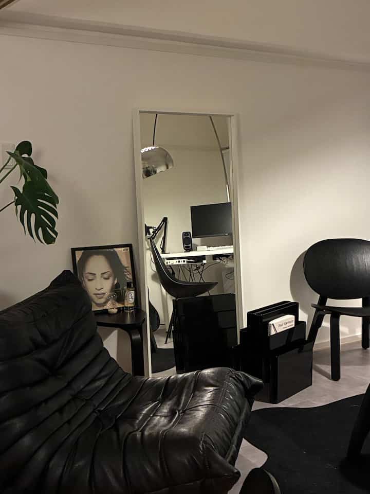 Monotone single household living room featuring black sofa and chair, with a home office visible in a mirror, creating a simple interior design