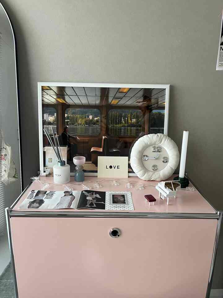 Simple Korean interior studio space featuring a pink storage cabinet with a framed poster, round clock, and minimal decor accessories creating a cozy atmosphere