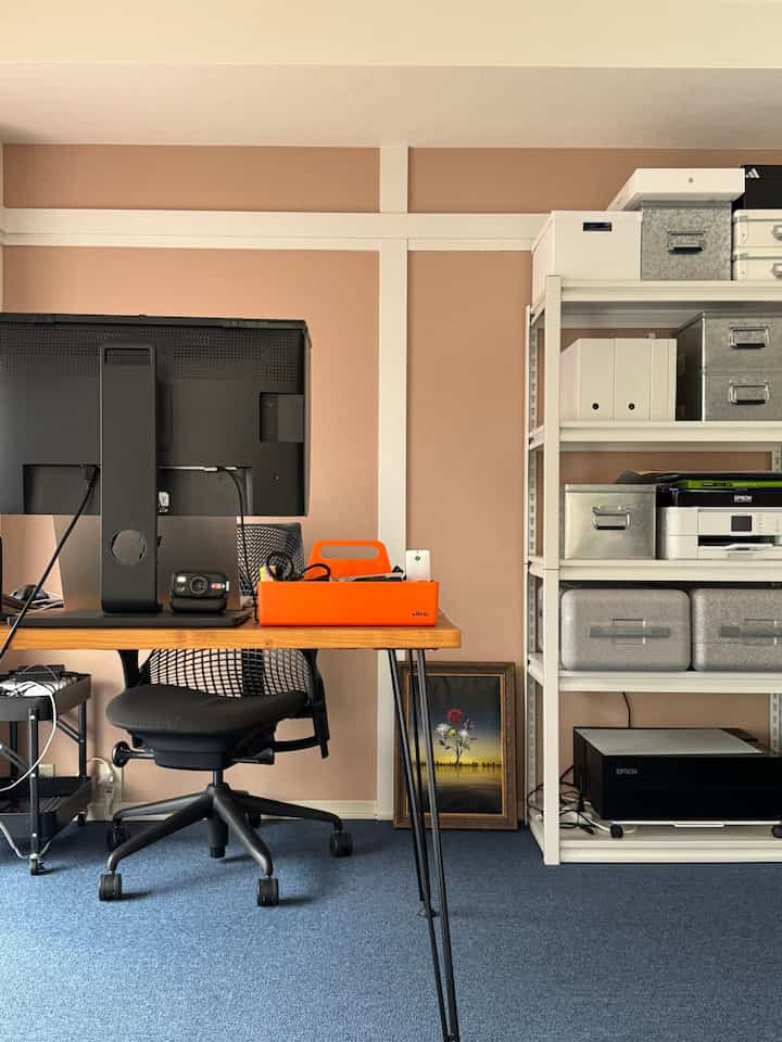 Warm brown walls and blue carpet define a home office with a black office chair and wooden desk creating a tidy workspace