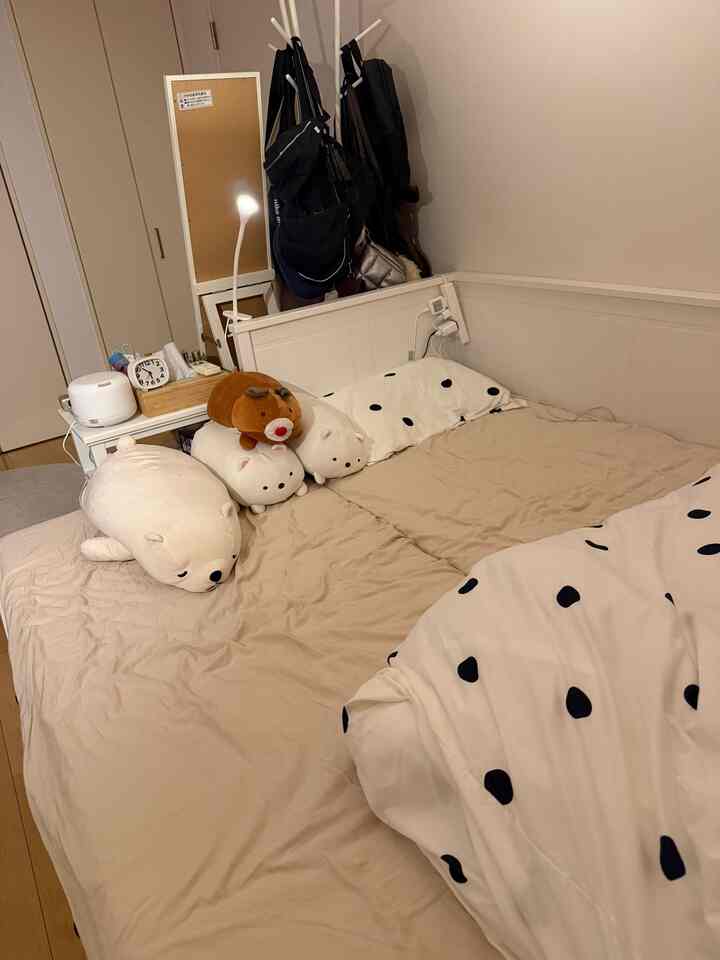 A cozy bedroom with white and beige tones, featuring a bed adorned with cushions and plush toys