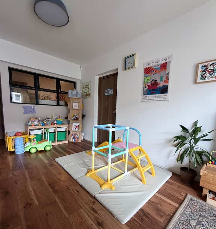 明るい白い壁と茶色の木製床の子供部屋、中央にカラフルな室内遊び場がマットの上に配置されたインテリア
