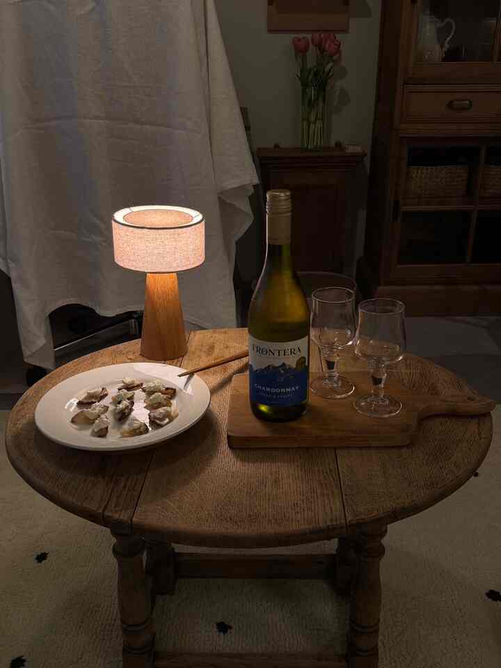 Warm brown wood tone living room with a wooden low table featuring a table lamp, a bottle of wine, and two wine glasses creating a cozy atmosphere