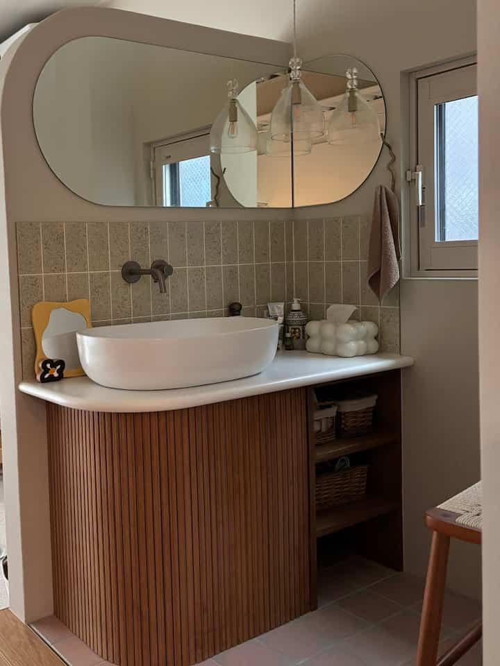 A cozy bathroom with natural tones and wooden vanity, featuring warm brown tiles and a large mirror for a relaxing atmosphere