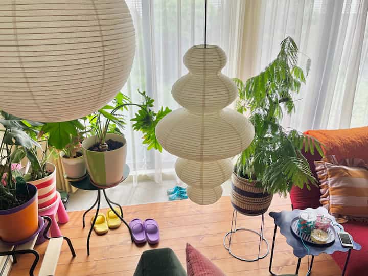 Natural color living room with white curtains and paper lamps, featuring various houseplants and cushions creating a warm atmosphere