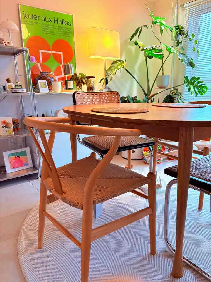 Light brown wood tone dining room featuring Y chair and wooden dining table with floor lamp and plants in cozy atmosphere