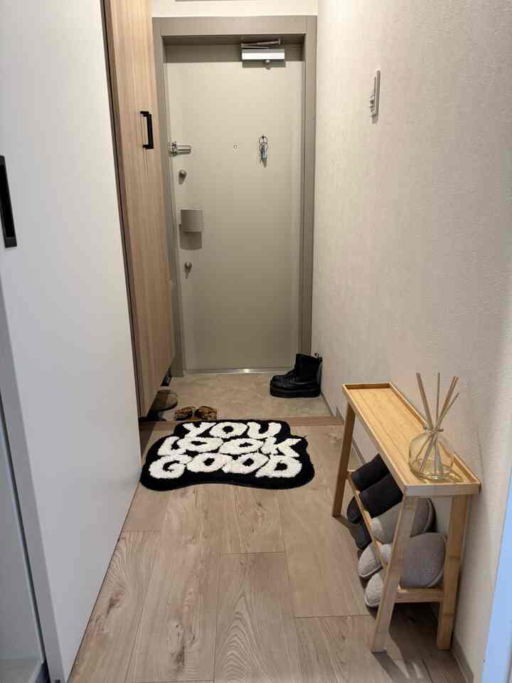 White and wood tone narrow entrance featuring a neat shoe rack and a patterned rug conveying a practical space