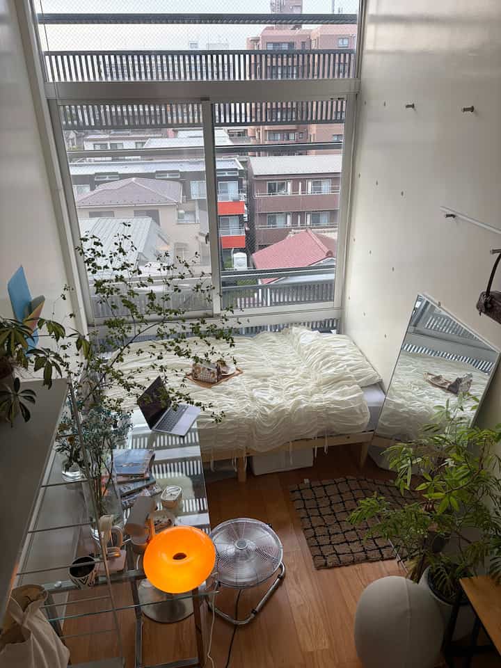 Bright white and natural wood-tone single bedroom featuring large windows and plants creating a natural atmosphere