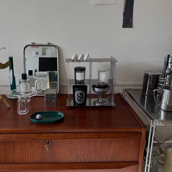 Natural kitchen space with brown wood-tone side table featuring silver metal shelf, assorted diffusers, candles, and coffee bean container