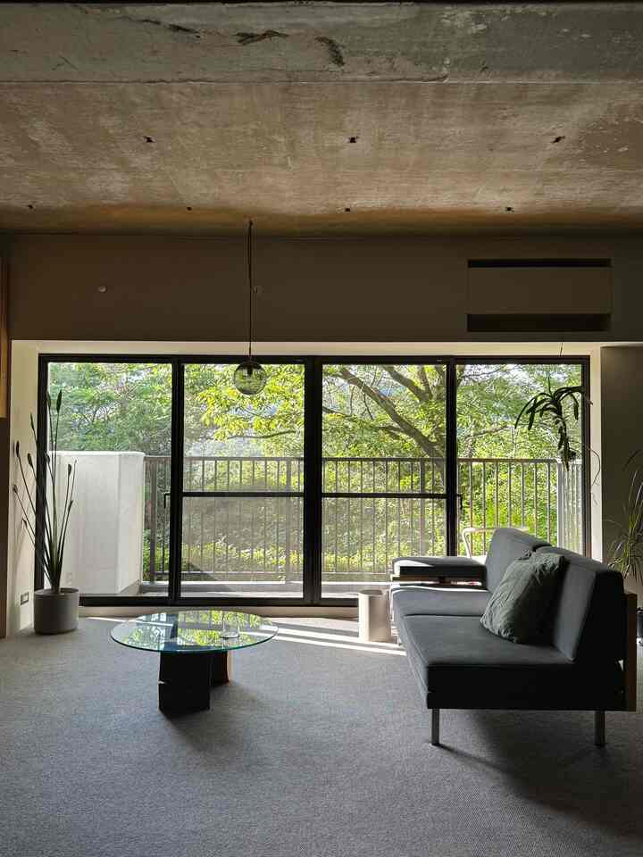 Natural-toned living room featuring a large window, modern dark gray sofa and a glass coffee table creating a cozy atmosphere