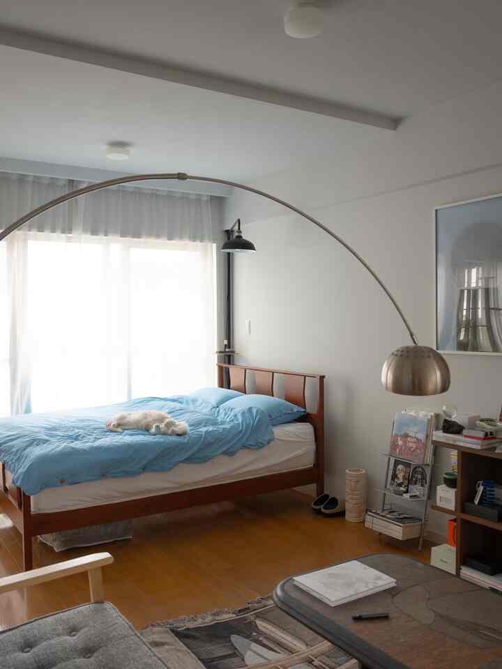 A white and blue toned bedroom featuring a wooden bed and floor lamp with a cat resting peacefully on the bed
