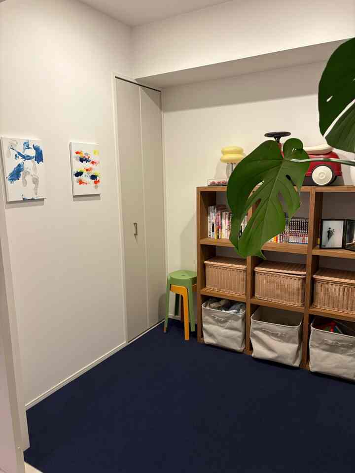 Kids' room with white walls and navy carpet, wooden bookshelf and stools, featuring children's artwork in a neat cozy space