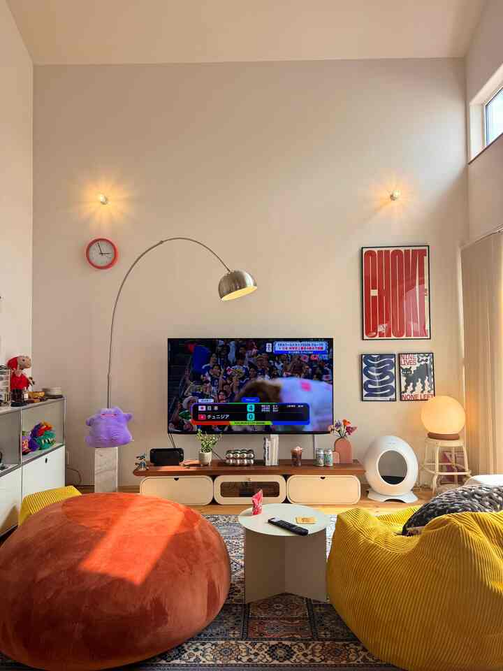 温かみのあるベージュとオレンジ色調のリビング、テレビや黄色いソファ、ペットハウスが配置された雰囲気のあるインテリア