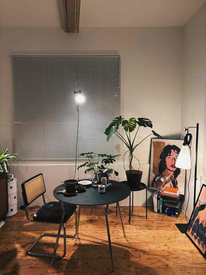 温かみのある木目調と植物が調和したモダンなダイニング、黒いダイニングテーブルとブラインドが配置されたシンプルな空間