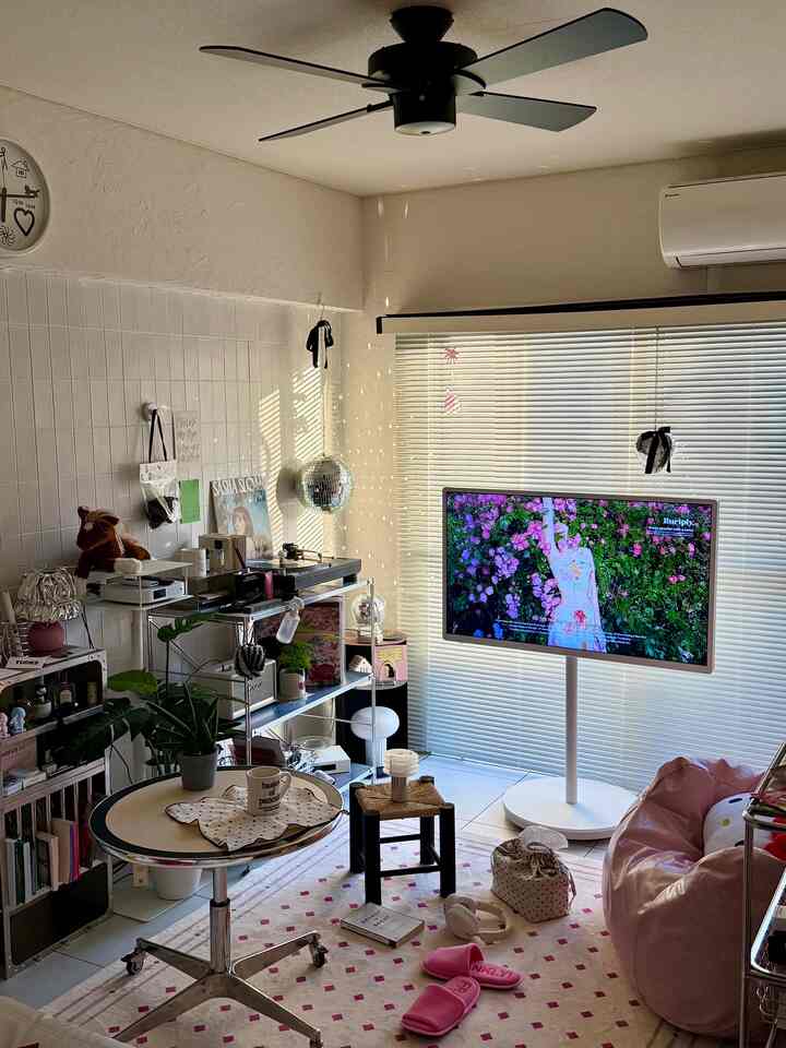 白い壁と床、ピンクのビーズクッションがあるリビングに、中央のスツールとテレビ台が配置されたシンプルなインテリア