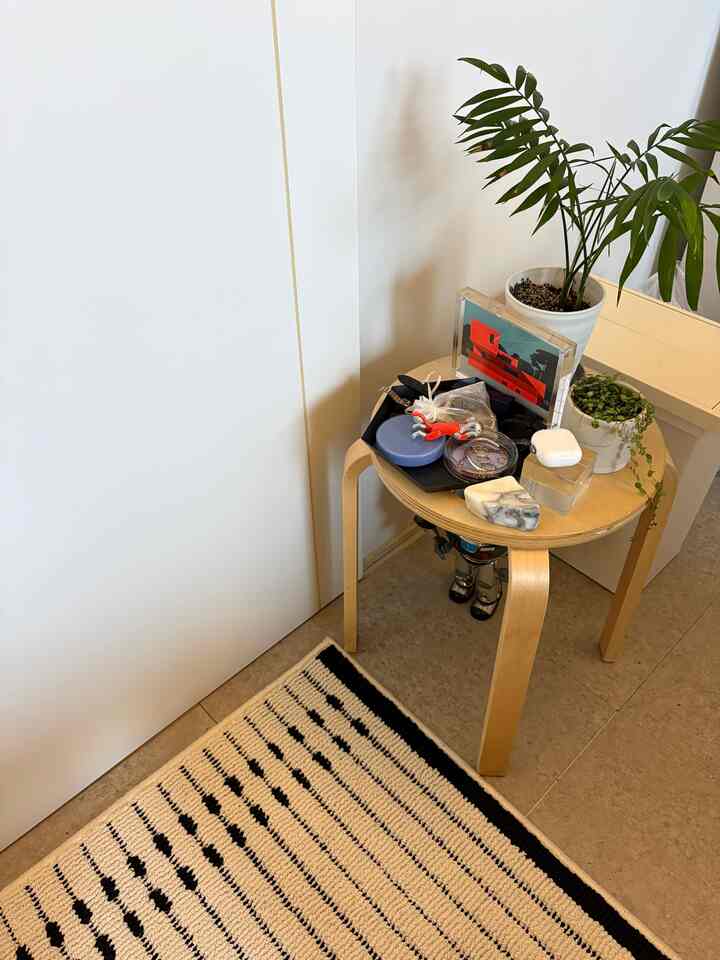 白い壁と木目調のスツール、トレイに植物が置かれたシンプルなワンルームのインテリア