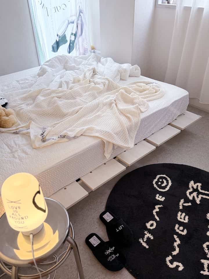 Bright white-toned bedroom featuring a central white bed with beige blankets in a simple setting