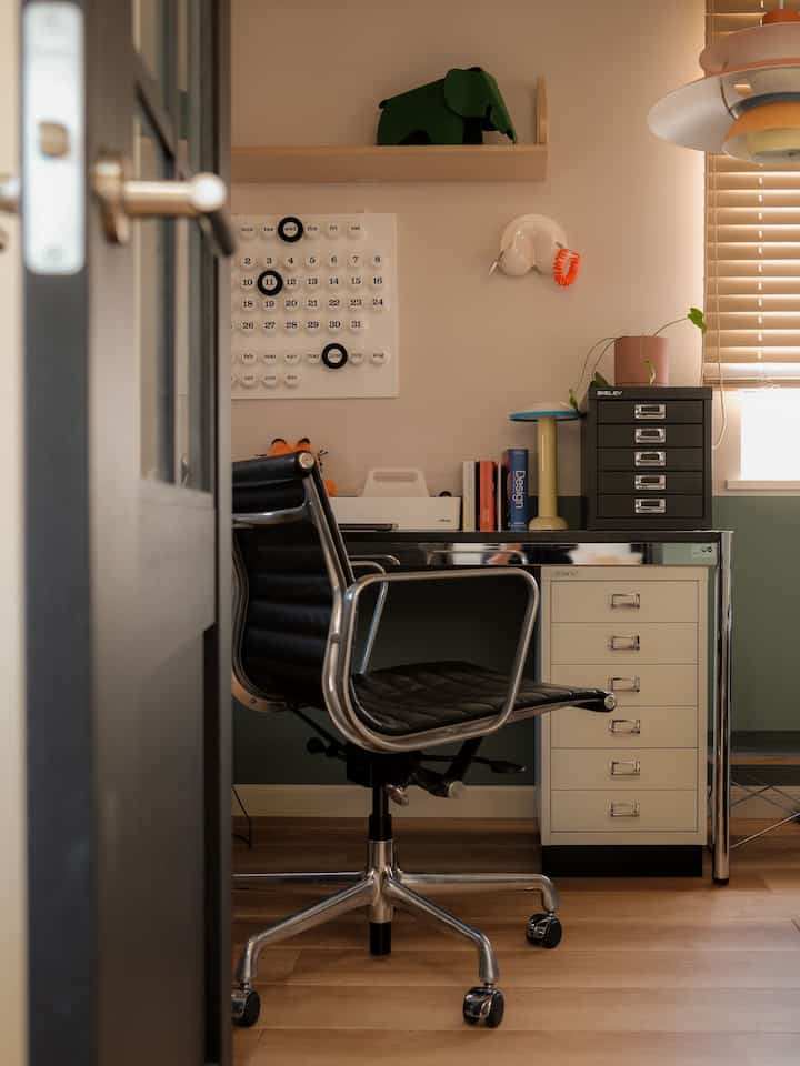 A home office in white walls and brown wood flooring featuring a black office chair, cabinet, and tidy desk in mid-century modern style