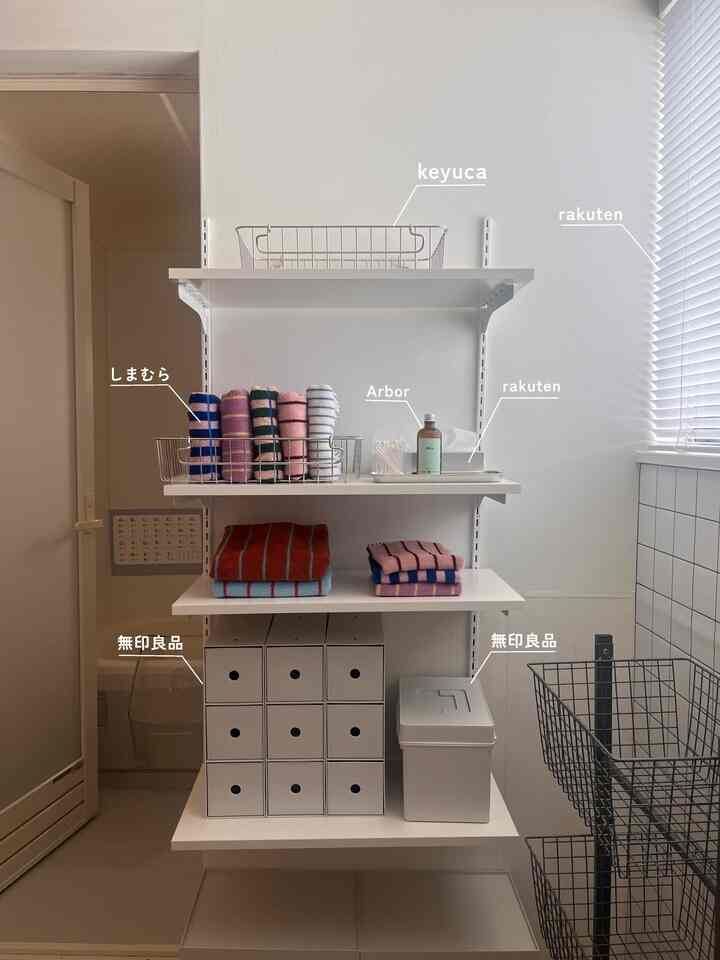 Bright white bathroom with minimalist storage shelving featuring MUJI boxes and neatly folded towels